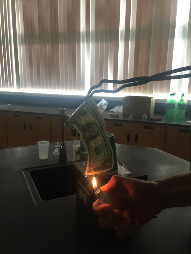 Expose the bottom of the bill to an open flame. You can use a lighter or a match for this. Thanks to my coworker for demonstrating this for the sake of me getting some good photos-- I'm sure you could imagine that me lighting the bill on fire while trying to simultaneously get a photo would not be very safe). 